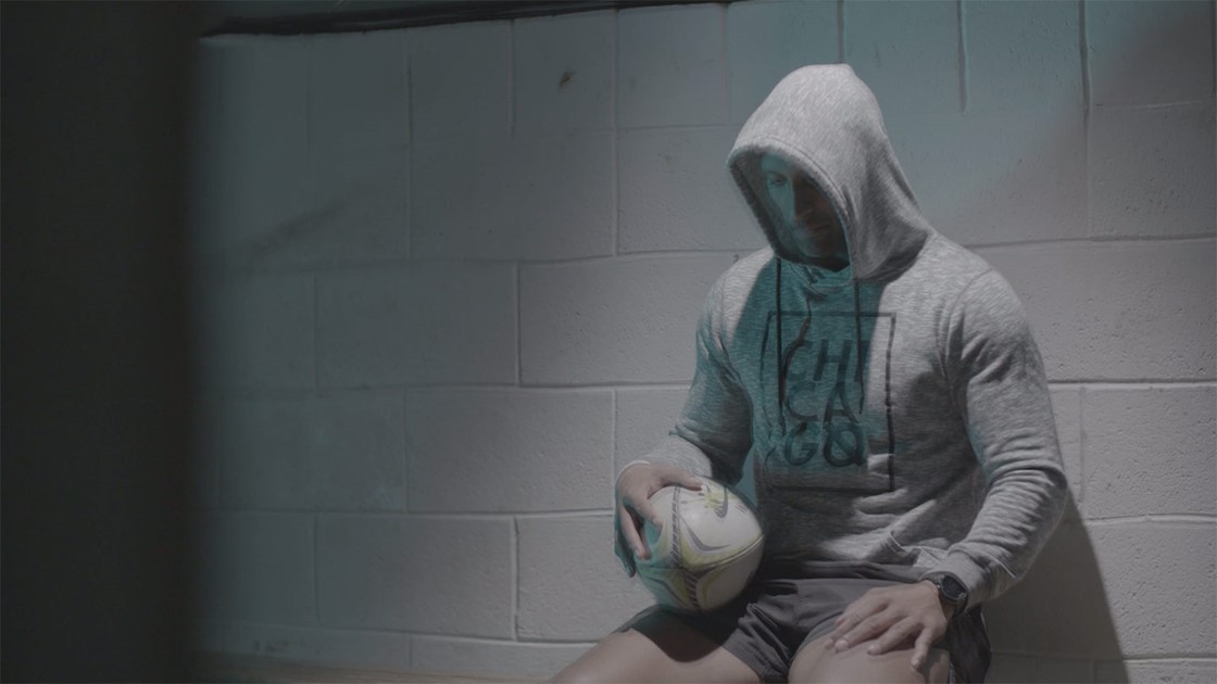 Paul hiding his face in a hoodie holding a rugby ball. 