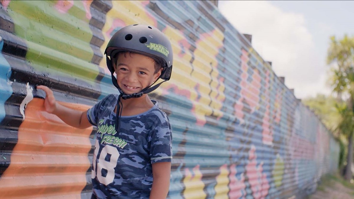 Ariki wearing a helmet in front of graffiti at the skatepark.