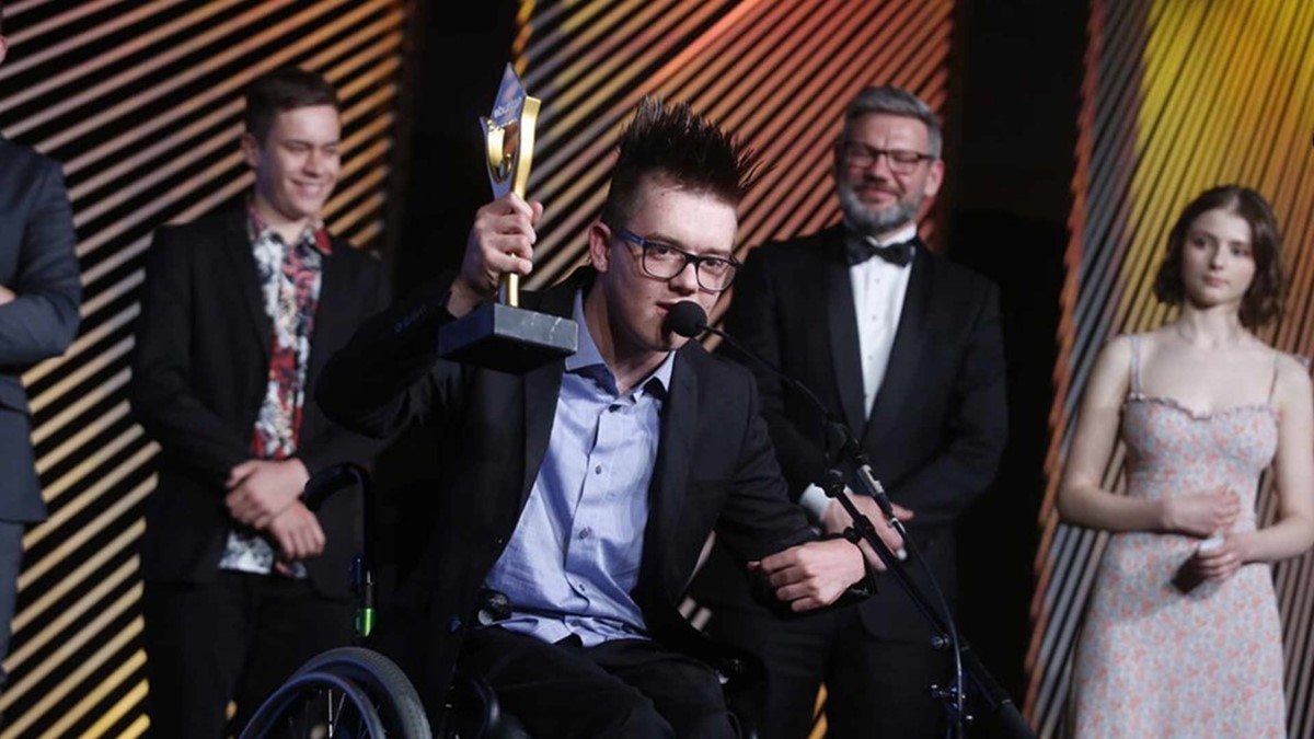 Cory Newman holding his award on stage.