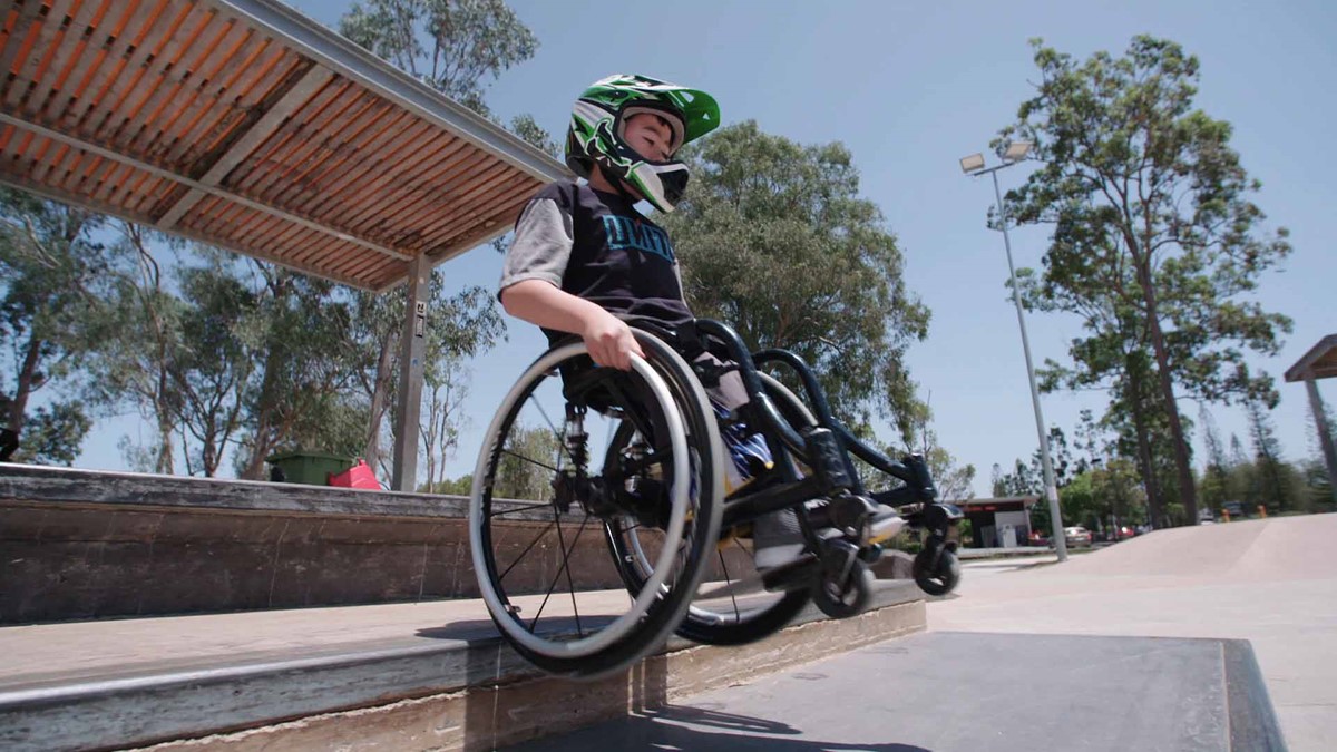 Josh jumbing off a curb in his wheelchair wearing a motorcross helmet.