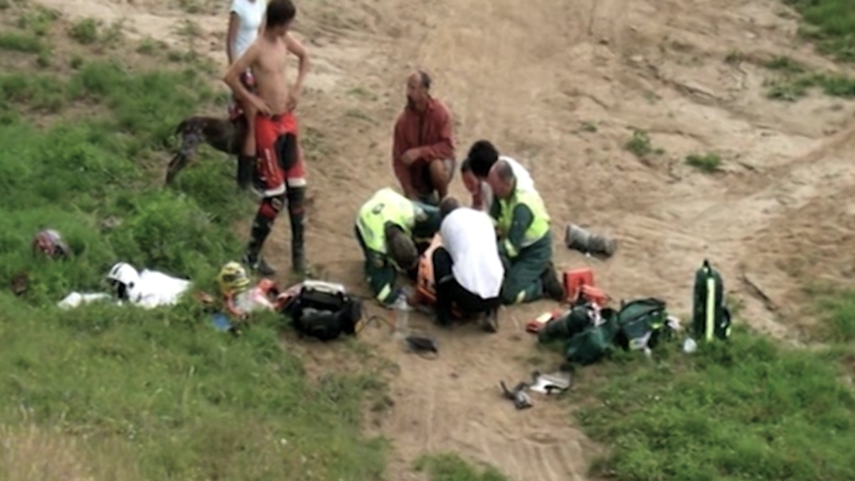 Scott lies on a dirt track, surrounded by medics as they assess his injuries